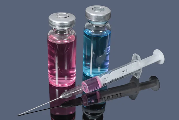 Медицинские ампулы с цветными вакцинами и шприц на темной бэкгру — стоковое фото