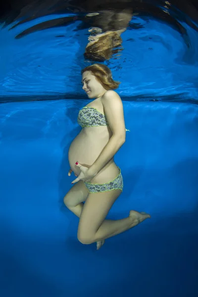 Young pregnant woman in a bikini under water in the pool