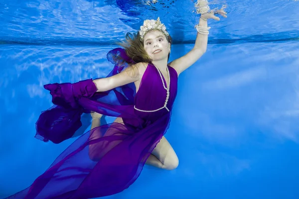 girl in long, lilac dresses wearing poses underwater