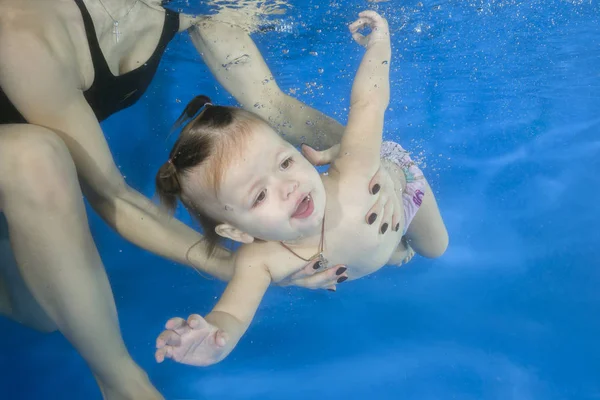 Little baby learning to swim underwater in a swimming pool, moth