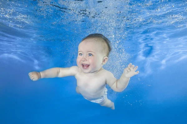 Funny face portrait of little baby girl swimming and diving underwater with fun in pool  on a blue water background. Healthy family lifestyle and children water sports activity.