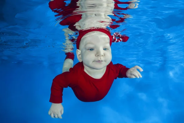 Funny face portrait of little baby boy in red costume swimming and diving underwater with fun in pool on a blue water background. Healthy family lifestyle and children water sports activity.