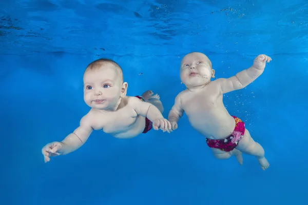 Two little baby swim in the pool on a blue water background. Healthy family lifestyle and children water sports activity. Child development, disease prevention
