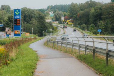 Metal korkuluklar ve yoğun yeşil ormanlarla çevrili kaldırımlı bir yolda, paralel yaya yolu ve yol kenarı işaretleri olan bir araç sürüyor..