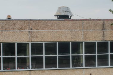 Düşük katlı bir sanayi binasında paslı bir çatı bacası ve ekmek reklamı ve dağıtım kamyonu gösteren yansıtıcı pencereler yer alıyor..