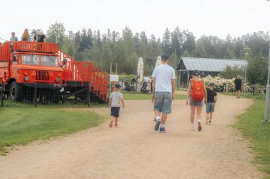 Birçok aile, ağaçlar, çiçekler ve küçük binalarla çevrili kırmızı itfaiye aracının yer aldığı bir eğlence parkında geziniyor. Rahat ve aile dostu bir ortam..