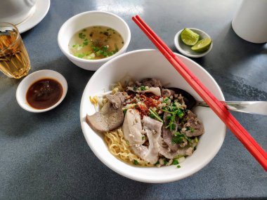 Domuz sakatatıyla kaplanmış kuru erişte tabağı, küçük bir kase temiz çorba ile servis edilir..