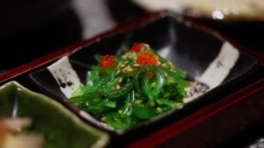 Japon yemek çubuklarının yakın çekimi zarif bir şekilde taze wakame yosunu topluyor, narin dokusunu ve canlı yeşil rengini vurguluyor. Bu otantik yemek pişirme anı yemek videoları, yemek tarifleri....