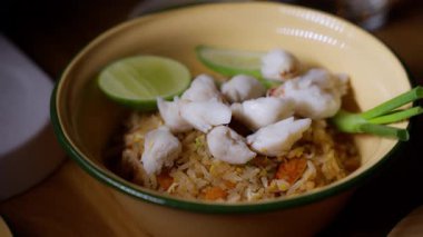 Yumuşak renkli kremalı bir kasede servis edilen, altın pirincin üstünde canlı bir yengecin yakın çekimi. Zengin dokular ve taze malzemeler gurme sunumunu ön plana çıkarıyor. Aşçılık videoları, deniz ürünleri restoranı..