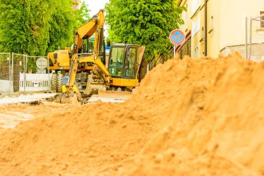 Şehirde bir inşaat alanı, turuncu tarak. Bölgedeki kanalizasyon inşaatı. Park edilmiş iş makinaları yolda. Buldozer Çekme Makinası. Bırakılan yol.