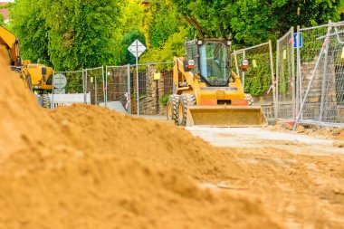 Şehirde bir inşaat alanı, turuncu tarak. Bölgedeki kanalizasyon inşaatı. Park edilmiş iş makinaları yolda. Buldozer Çekme Makinası. Bırakılan yol.