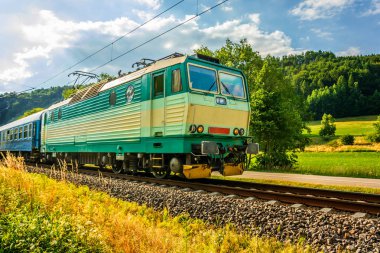 Çek kırsal geçen yeşil elektrikli lokomotif. Yeşil vadi boyunca çalışan bir tren. Taşıma Çek Cumhuriyeti'nde demiryolu. Demiryolu güneşli bir günde. Kırsal bir platform üzerinde gelen tren