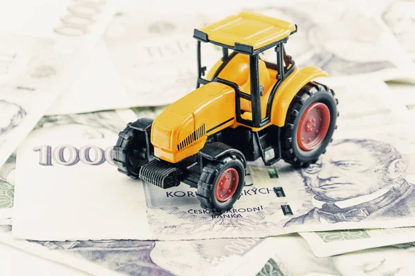 A tractor toy on banknotes as a concept of buying or renting a tractor. Loan for buying a tractor. Czech money at the table. Financial concept with money.