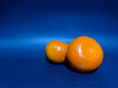 İki parlak turuncu portakal, mavi arka planda hafif parlak portakal kabuğu dokusu..