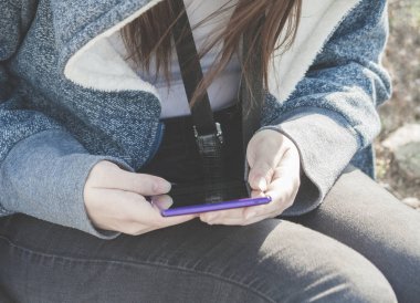 kızı lila rengi elinde büyük bir telefon ile oturuyor, tarçın-kırmızı saçlarını Rüzgar, mavi bir ceket, bir güneşli gün, coşku geliştiriyor