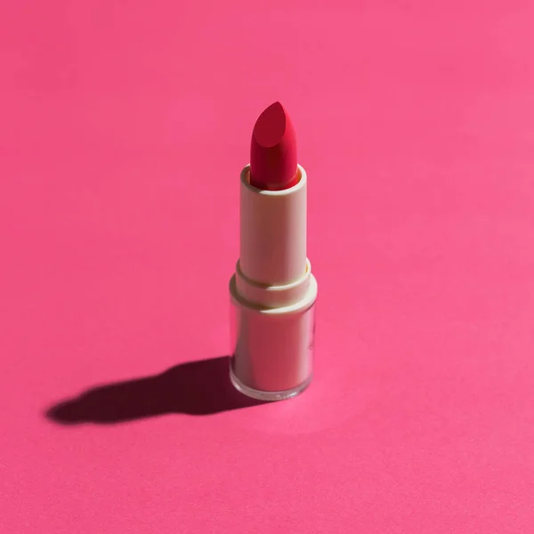 Brand new red tinted lipstick in studio light flat lay on pink background.