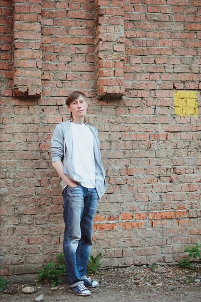 young man  in casual clothing standing in full size near brick wall background