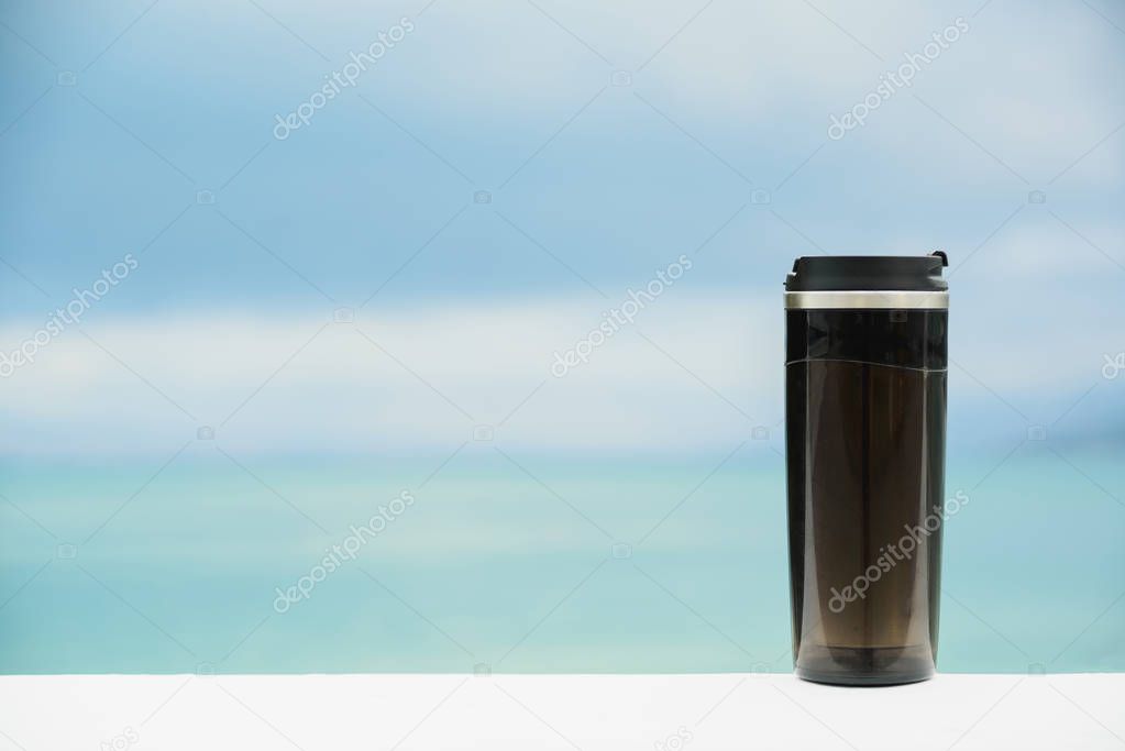 plastic black thermos mug without handle on blurred sea and sky 