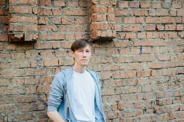 Genç yetişkin adam grange kırmızı tuğla duvar arka planında duruyor.