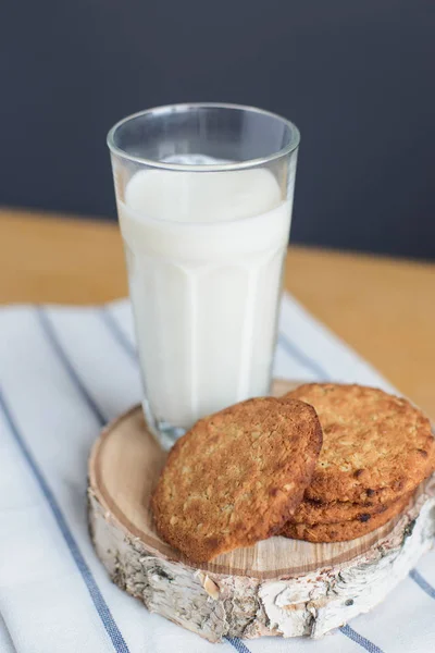 Στρογγυλό καφέ μπισκότα ολικής άλεσης και γυαλί γάλακτος σε ριγέ λευκή πετσέτα σε ξύλινο τραπέζι — Φωτογραφία Αρχείου