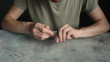 Adam altın kanca ve gri pamukla örgü örmeye başlıyor. Taş masa üstünde, ön cephede. Gerçek zamanlı HD stok video görüntüleri.