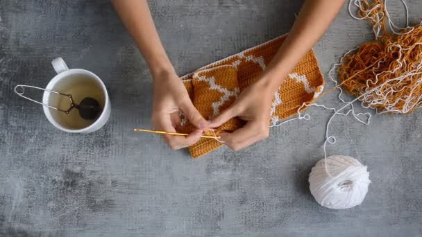 大人女の子手かぎ針編みフックともにオレンジと白の綿の糸で石のテーブルの上の背景 上からのビューアップフルHdストックビデオビデオビデオのリアルタイム — ストック動画