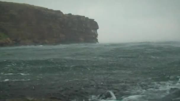 Chuva forte na superfície do mar contra o pano de fundo de uma costa rochosa, tiro largo . — Vídeo de Stock