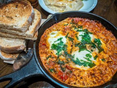 Shakshouka 'nın en iyi manzarası, kızartma tavasında haşlanmış yumurta ve Suudi Arabistan' ın Riyad kentindeki yerel bir restoranda yemek masasında ekmek..