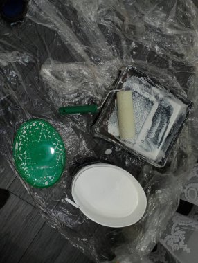 Evde tamirat var. Yere bir polietilen film serilir, üzerinde duvarları boyamak için bir silindir ve yanında büyük bir kova beyaz boya olan bir tepsi bulunur..