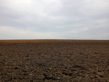 Ufukta gri kasvetli bir gökyüzüne dönüşen sabanla sürülmüş bir tarlanın manzarası. İlkbaharda tarım ve arsa konuları.