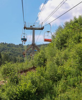 Bir kayak asansörü ağaçlar ve çalılarla kaplı bir dağ yamacına tırmanır. Güneşli bir yaz günü mavi gökyüzü ve açık bulutlar turistler için pitoresk bir manzara yaratır..