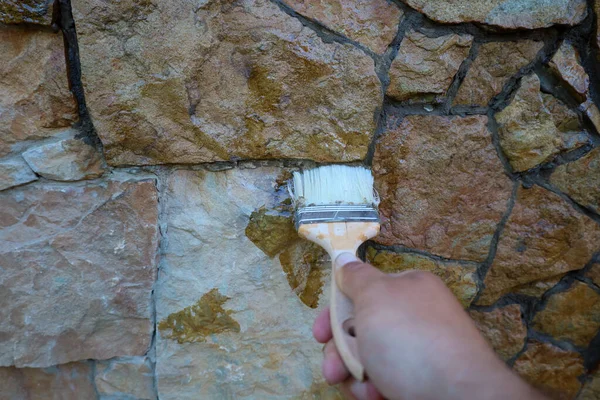 Doğal taşlardan inşa edilmiş taş bir duvar, bir fırça kullanılarak koruyucu bir kaplamayla kaplanıyor. Bu süreç yüzeye zengin bir renk, derin bir doku ve doğal maddenin güzelliğini vurgulayan karakteristik bir parıltı verir..