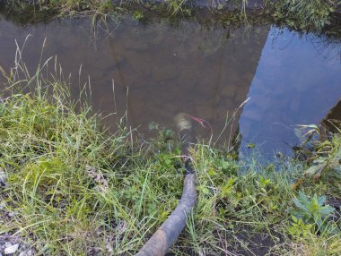 Suya batırılmış bir hortum derin bir çukurdan su pompalama işlemini gösterir. Görüntü, çalışan bir atmosferi taşır ve bir su sorununa mühendislik çözümü gösteren teknik tarafı vurgular..