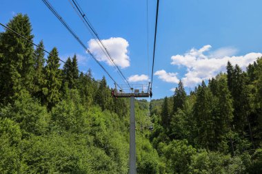 Yoğun bir ormanın üzerinden geçen bir teleferik macera ve seyahat hissi yaratır. Bu görüntü, mühendislik teknolojisiyle doğanın güzelliğini birleştiriyor. Çevredeki tepelerin muhteşem manzarasını sunuyor..