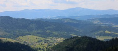 Mavi ufukla birleşen görkemli dağ sırtlarının panoramik görüntüsü. Aralarındaki vadiler sık ormanlarla kaplıdır ve vadiler bu manzarayı büyüleyici ve büyüleyici yapan küçük köylerle doludur..