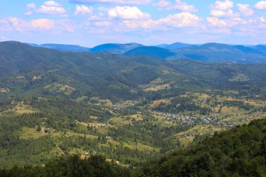 Vadilere yerleşmiş küçük köyleri olan ormanlarla kaplı görkemli bir dağ manzarası. Görüntü, doğa ve insanların barışçıl ve sakin bir şekilde bir arada yaşadıklarını gösteriyor. Dağların katmanlı görüntüsü uzaklarda kayboluyor. 