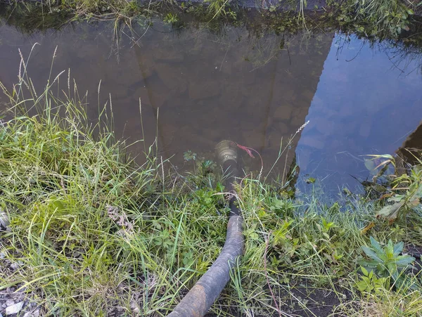 Suya batırılmış bir hortum derin bir çukurdan su pompalama işlemini gösterir. Görüntü, çalışan bir atmosferi taşır ve bir su sorununa mühendislik çözümü gösteren teknik tarafı vurgular..