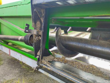 Bir biçerdöverin çalışma mekanizmasına yakın plan, güçlü bir çapa ve toz ve bitki artıklarıyla kaplı diğer ayrıntıları gösteriyor. Bu görüntü, alandaki sıkı çalışmanın gerçekçi atmosferini yansıtıyor ve gücü vurguluyor. 