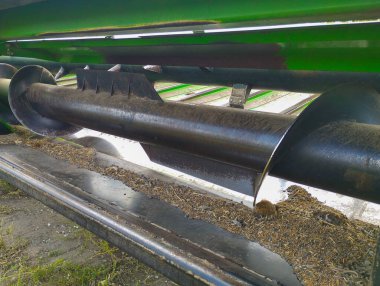 Endüstriyel görünüşünü, iş izlerini ve bitki artıklarını gösteren bir biçerdöverin içindeki büyük çaplı bir çapa yakın plan. Bu ayrıntı, zorlu koşullarda çalışan tarım makinelerinin gerçekçiliğini ve gücünü aktarır..