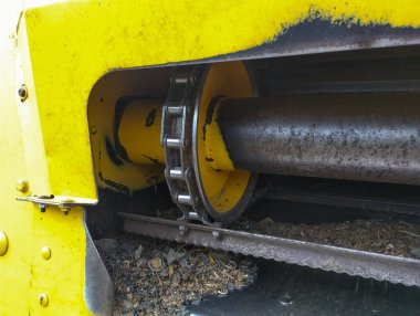 Bir kombinasyon mekanizmasındaki büyük metal bir zincir ve teçhizatın yakın çekimi. Detaylar, pas ve tozla, makinenin yoğun çalışmalarını vurguluyor, ağır iş gücü ve tarım üretiminden oluşan bir atmosfer yaratıyor.