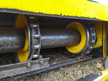 Hasat makinesinin mekanizmasına yakın çekim. Devasa metal parçalarını, dişlileri ve zincirlerini gösteriyor. Görüntü, çok çalıştığını gösteren pas ve kir izlerini ortaya çıkarıyor ve tarım makinelerinin gücünü ve güvenilirliğini vurguluyor..