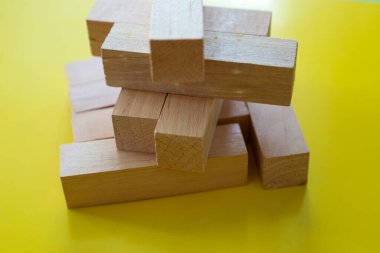 Tahta bloklardan oluşan dengesiz bir yapı, kırılganlığı ve riski simgeliyor. Sarı arka plan görsel zıtlığı arttırarak bileşimi dinamik ve dikkat çekici kılıyor..