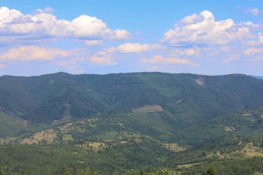 Uçsuz bucaksız mavi gökyüzünün altındaki yemyeşil ormanlarla kaplı görkemli dağların nefes kesici manzarası. Bu panorama vadideki vahşi doğa ve küçük yerleşim alanlarının ahenkli bir karışımını gösteriyor..