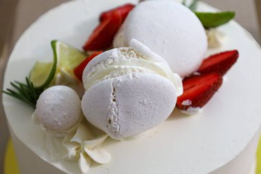 Taze çilek parçaları, beyaz krema ve limon dilimleriyle süslenmiş beyaz bir pastanın yakın çekimi tazelik ve sofistike bir hava yaratıyor..