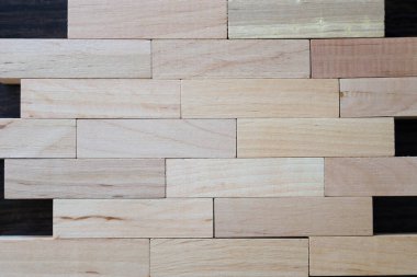 Tahta bloklar, sıkıca istiflenmiş, koyu arkaplanda dikdörtgen bir duvar oluşturuyorlar. Fotoğrafta odunun doğal dokusu ve gölgesi görülüyor..