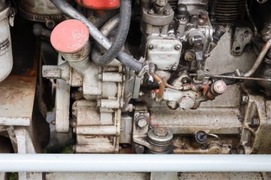 Çok sayıda mekanizma, boru ve cıvata gösteren eski, kirli bir motorun parçası. Çekim, teknik aşınma, ağır iş ve endüstriyel estetik atmosferi taşır..