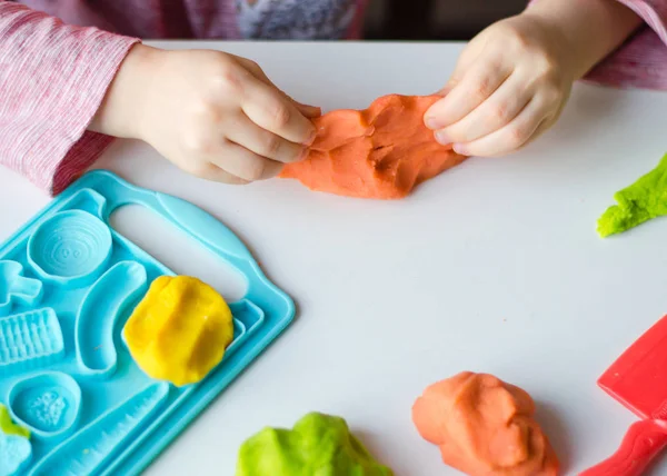 Child hands playing with colorful clay. Homemade plastiline. Plasticine.  play dough. Girl molding modeling clay. Homemade clay. Stock Photo