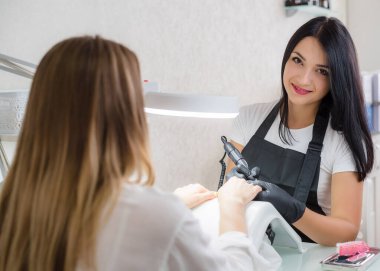 Manikür ustası kız, güzellik salonundaki bir müşteriye manikür yapıyor. Tırnak uzatıcısı, cila.