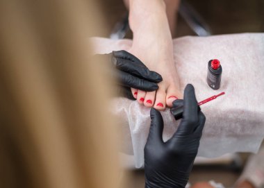 Pedikür uzmanı müşterinin tırnaklarını kırmızı cila ile boyuyor. Yakın plan..