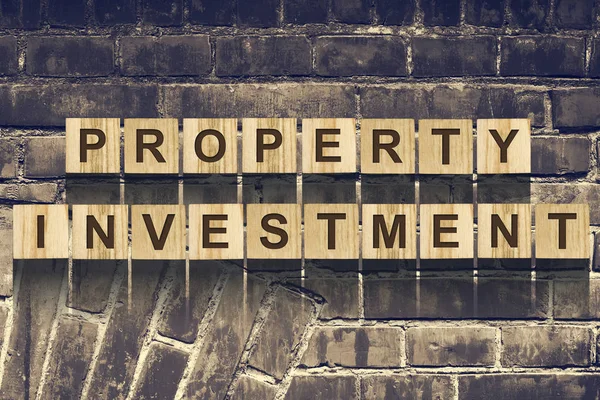 Ord, fastighetsinvesteringar, bestående av bokstäver på träkonstruktion kuber mot bakgrund av en gammal vintage tegelvägg. Konceptet business — Stockfoto